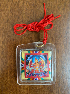 A square shaped amulet of the Loving Mother, Sherab Jamma. A red thread is attached to the amulet by a metal ringlet so it could be worn. The image of Sherab Jamma inside the amulet is colorful and decorated with thread details on the back. The amulet has smooth edges.